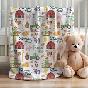May include: A white fleece blanket featuring a repeating farm-themed pattern of red barns, green tractors, cows, pigs, horses, chickens, scarecrows, hay bales, and yellow suns. The text Thomas Reid is printed in green and brown throughout the design.