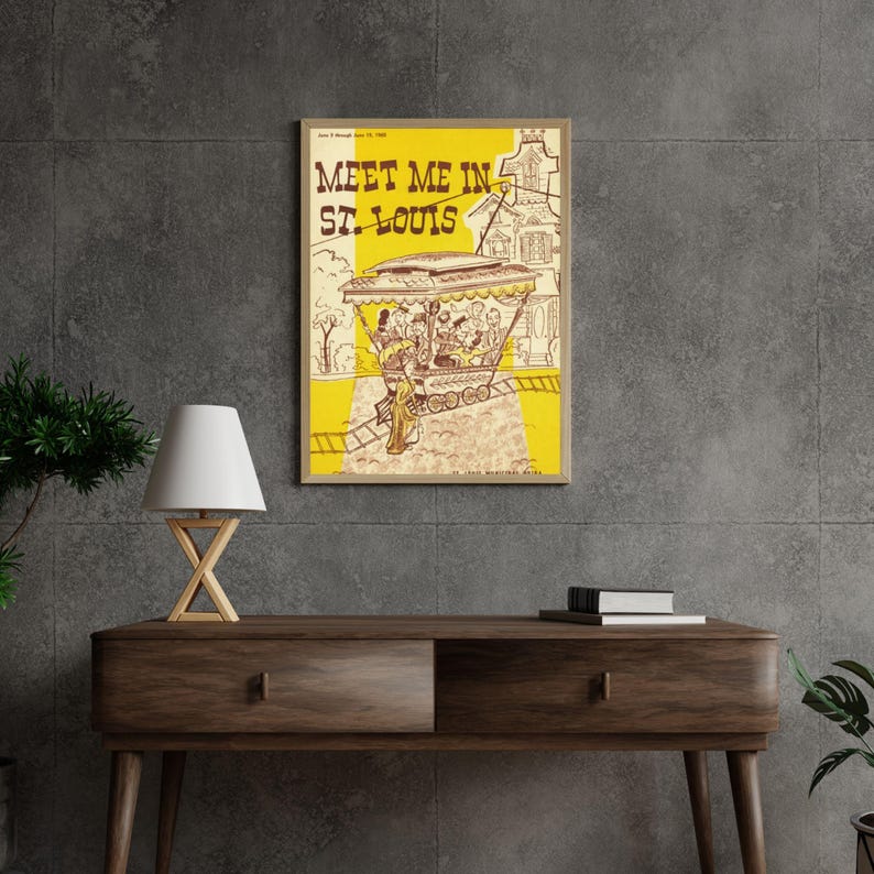 May include: Framed vintage poster with the text "Meet Me in St. Louis" in bold letters. The poster features a yellow background with an illustration of a trolley car and people. The poster is displayed on a dark wood console table.