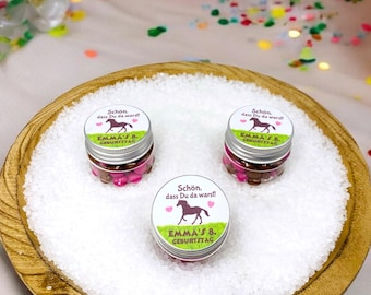 Op de afbeelding: Drie kleine glazen potjes gevuld met roze en bruine snoepjes. Elk potje heeft een wit etiket met een bruine paardenillustratie en de tekst "Schön. dass Du da warst!" en "EMMA'S 8. GEBURTSTAG". De potjes staan op een houten dienblad gevuld met wit zand.