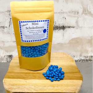 Puede incluir: Una bolsa de lentejas de chocolate azules etiquetada "Vollmich Mini Schokolinsen" con el texto "Zum einfach so naschen oder dekorieren von Kuchen 400 Gramm".