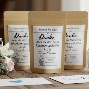 Op de afbeelding: Drie kraftpapieren zakjes met witte etiketten met de tekst "Danke" en een bloemenillustratie. Een klein boeket bloemen en een vetplant in een witte pot zijn ook aanwezig.