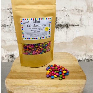 Puede incluir: Una bolsa marrón de mini caramelos de chocolate de colores. La bolsa está etiquetada como "Vollmich Mini Schokolinsen" y dice "Zum einfach se naschen oder dekorieren von Kuchen" y "400 Gramm".