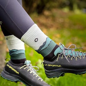 Könnte beinhalten: Ein Paar schwarze Wanderschuhe mit grünen Schnürsenkeln und dem Schriftzug "LA SPORTIVA" an der Seite. Die Schuhe werden mit weißen und grünen Socken getragen.