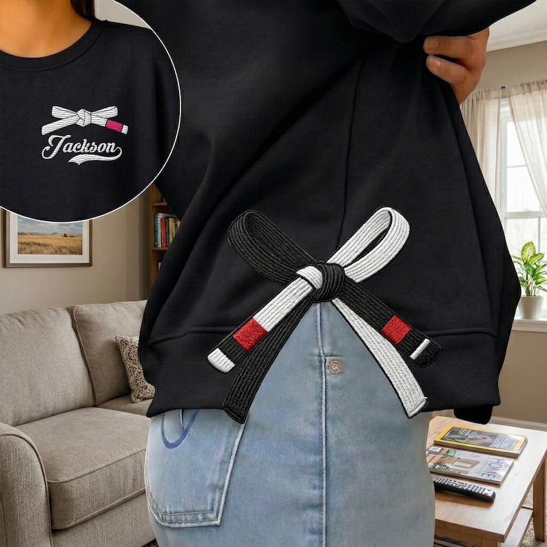 Peut inclure: Sweat-shirt noir avec un motif de ceinture de Jiu-Jitsu brod&eacute;. La ceinture est noire et blanche avec des accents rouges. Le sweat-shirt porte &eacute;galement le nom "Jackson" brod&eacute; en blanc.