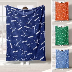 May include: A blue fleece blanket with a white hockey stick and puck pattern. The blanket has the name "JACKSON" repeated throughout the pattern.