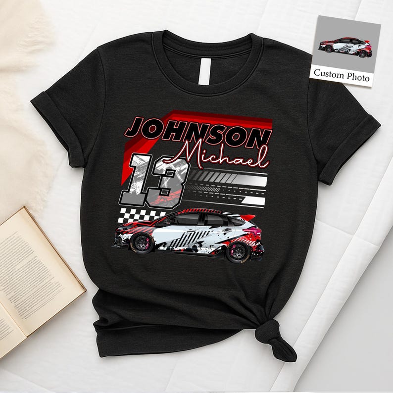 May include: Black t-shirt with a race car design. The shirt features the name "Johnson Michael" and the number "13". The car graphic is white, red, and black. A small image of the car is in the upper right corner.