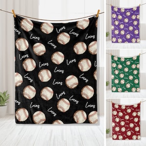 Puede incluir: Una manta de franela negra con un patrón repetido de pelotas de béisbol y el nombre "Lucas" escrito en cursiva blanca. La manta se muestra doblada y colgada de un tendedero.