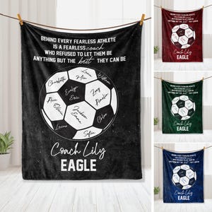 Könnte beinhalten: Eine schwarze Fleece-Decke mit einem weißen Fußball-Design. Der Fußball hat auf jedem Panel Namen geschrieben. Der Text "Behind every fearless athlete is a fearless coach who refused to let them be anything but the best they can be" befindet sich oben auf der Decke. Der Text "Coach Lily Eagle" befindet sich unten auf der Decke.