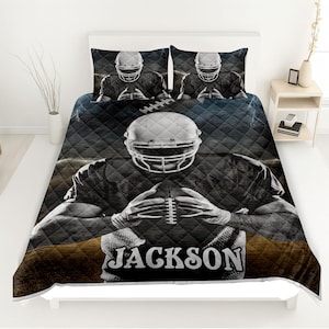 May include: A black and white football-themed quilt set featuring a football player holding a football. The quilt and two pillowcases display a grid pattern. The name "JACKSON" is printed on the quilt.