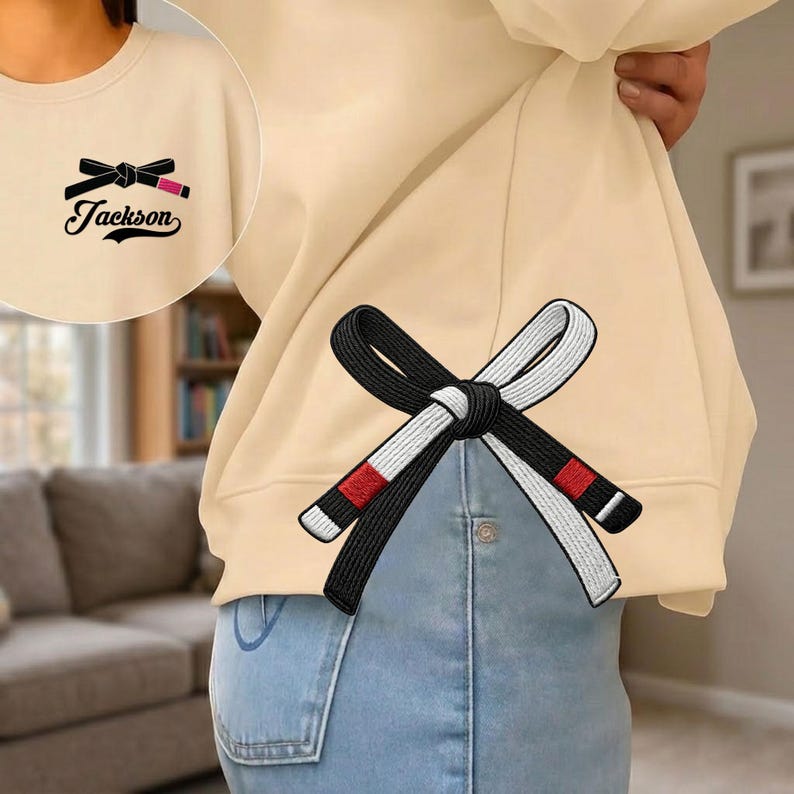 Peut inclure: Sweat-shirt beige avec un motif de ceinture noire et blanche dans le dos. Le devant pr&eacute;sente un motif de rouge &agrave; l&egrave;vres et de n&oelig;ud avec le nom "Jackson". Le sweat-shirt est port&eacute; avec un jean bleu.