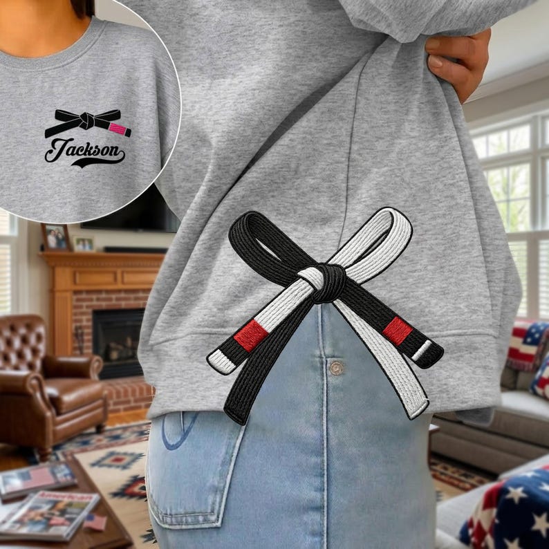 Peut inclure: Sweat-shirt gris avec un motif de ceinture de Jiu-Jitsu brod&eacute; en noir et blanc au dos. Le devant pr&eacute;sente une version plus petite du motif de la ceinture et le nom "Jackson". Le motif comprend une ceinture noire avec des rayures rouges.