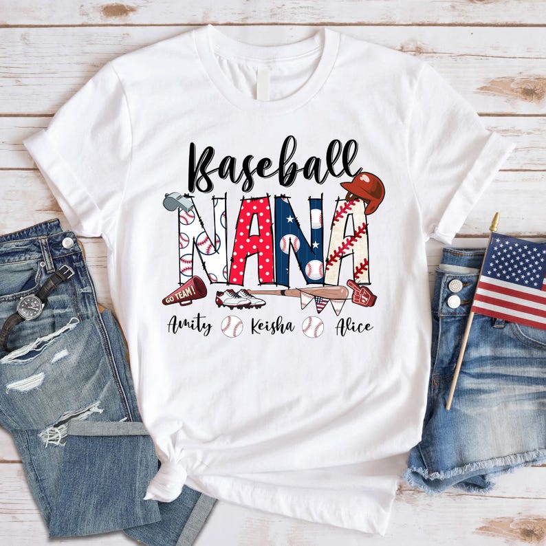 Puede incluir: Camiseta blanca con el texto "Baseball Nana" en rojo, blanco y azul. El texto est&aacute; decorado con pelotas de b&eacute;isbol, bates y otros gr&aacute;ficos de tem&aacute;tica de b&eacute;isbol. Los nombres "Amity", "Keisha" y "Alice" est&aacute;n impresos debajo del texto principal.