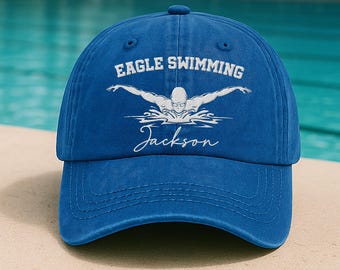 May include: A blue baseball cap with the text "EAGLE SWIMMING" and a swimmer graphic. Below the graphic is the name "Jackson" in a script font. The cap has a curved brim and a classic six-panel design.