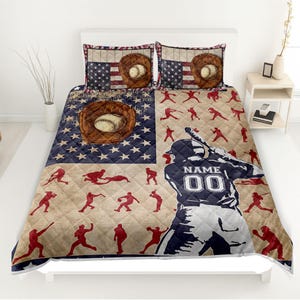 May include: Baseball-themed quilt set featuring a baseball player silhouette, baseball gloves, and baseballs. The design incorporates the American flag with stars and stripes. The set includes a quilt and two pillow shams.
