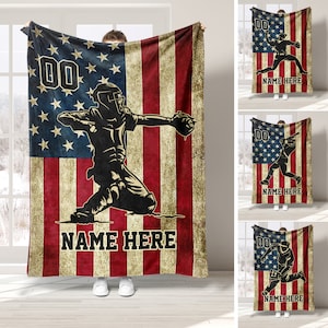 Puede incluir: Una manta de forro polar personalizada con la silueta de un jugador de béisbol frente a una bandera estadounidense. La manta tiene un aspecto desgastado y el texto "NAME HERE" está impreso debajo del jugador.