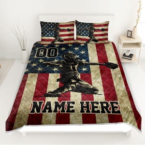 May include: A baseball-themed bedding set featuring an American flag design. The set includes a quilt and two pillowcases. The quilt showcases a baseball player silhouette, the number "00", and the text "NAME HERE". The color scheme is red, white, and blue.