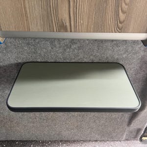 May include: A light grey folding table with a black trim, mounted to the wall inside a vehicle.