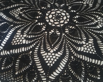 May include: Black crocheted doily with a circular design featuring a central flower and intricate patterns.