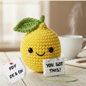 May include: A crocheted lemon with a smiling face, black eyes, and pink cheeks. It has a green leaf and a small white tag that says "YOU GOT THIS!". A second note says "PDF DE & EN".