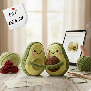 Puede incluir: Dos peluches de aguacate de ganchillo, uno sosteniendo un hueso marrón, con caras sonrientes y mejillas rosadas. Una tableta muestra un patrón de aguacate. Una nota dice "Happy Valentine's Day". También hay hilo verde y rosas rojas de ganchillo.