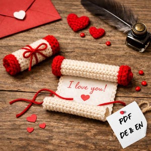 Könnte beinhalten: Romantische Szene mit einer gehäkelten Schriftrolle mit dem Text "I love you!" und einem Herz, zusammen mit roten gehäkelten Herzen und einem roten Umschlag mit einem Herz. Eine dekorative Feder und ein Tintenfass sind ebenfalls vorhanden.