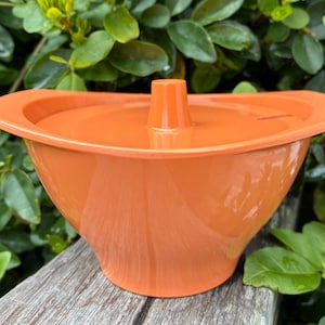 May include: A bright orange plastic bowl with a matching lid featuring a central handle. The bowl has a wide, flared rim and a tapered base, presenting a smooth, solid-colored surface throughout the entire kitchen container design.