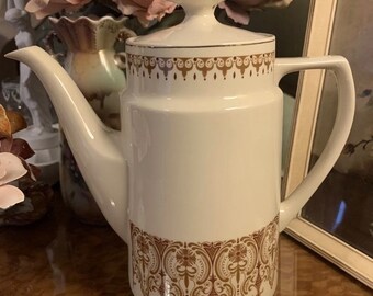 May include: A white ceramic coffee pot with a gold trim and brown floral pattern. The pot has a lid and a handle.