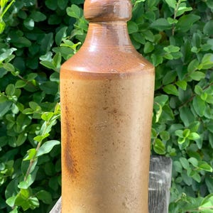 May include: A tall, brown stoneware bottle with a rounded top. The bottle has a rustic, aged appearance.