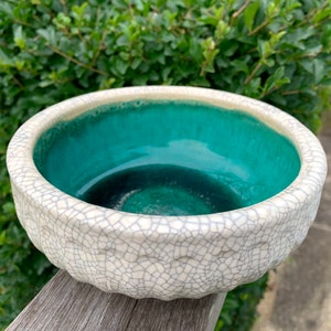 Może przedstawiać: Biała ceramiczna doniczka z pękniętą glazurą i turkusowym wnętrzem. Doniczka jest okrągła i ma szeroki rant.