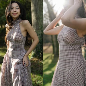 May include: A halter-neck plaid dress in shades of brown, pink, and black. The dress features a fitted bodice and a flared skirt. The fabric has a classic check pattern. The dress is suitable for a variety of occasions.