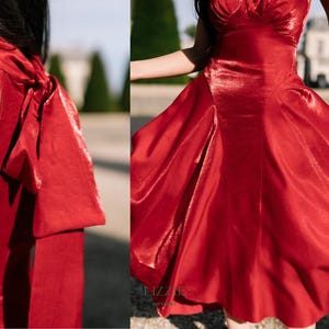 May include: A bright red dress with a flowing skirt and a high neckline. The dress has a large bow detail at the back and is made of a shiny, silky material. The dress is suitable for formal events.