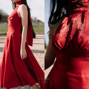 May include: A striking red dress with a high neck and a flowing skirt. The dress has a halter-style top and a bow detail at the back. The dress is made of a shiny fabric, suitable for formal events.