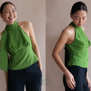 May include: A green halterneck top with a high neckline and a flowing sash detail. The top has a fitted bodice and is paired with black trousers. The image shows the top from multiple angles.