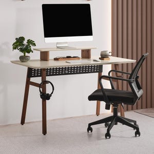 May include: A modern home office setup featuring a desk with a computer monitor, a black office chair, and a small potted plant. The desk has a light-colored top and dark wooden legs. A shelf with decor is mounted on the wall above the desk.