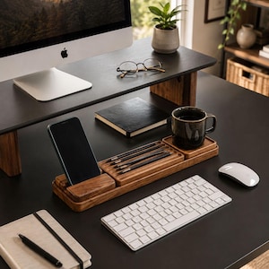 May include: A dark wood desk organizer set featuring a vertical smartphone stand, a rectangular tray with four black pencils, and a square coaster holding a dark ceramic mug. The organizer sits on a black desk surface near a white keyboard.