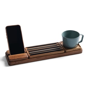 May include: A rectangular wooden desk organizer featuring a slot for a smartphone, a recessed tray holding four black pencils, and a square coaster section supporting a solid light blue ceramic mug with a handle, all crafted from dark wood.