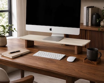 Könnte beinhalten: Ein Monitorständer mit einer glatten, hellen, rechteckigen Oberfläche, die von zwei dunklen Holzbeinen getragen wird. Der Ständer steht auf einem Schreibtisch aus Holz und trägt einen silbernen Computermonitor mit schwarzem Bildschirm und Apple-Logo.