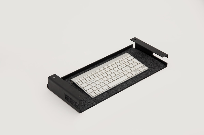 K&ouml;nnte beinhalten: Ein schwarzes Metall-Tastaturfach mit grauer Filz-Auskleidung. Eine wei&szlig;e drahtlose Tastatur liegt auf dem Fach.