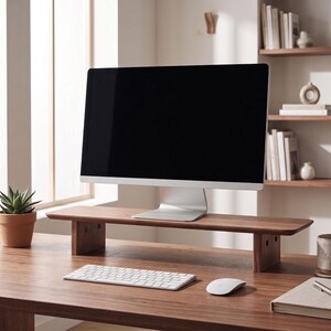 May include: A rectangular dark wood monitor stand with a smooth surface and two sturdy side supports. The stand is positioned on a wooden desk, holding a silver computer monitor, with a white keyboard and mouse placed in front of the stand.