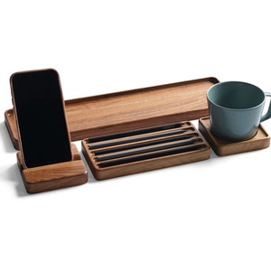 May include: A wooden desk organizer set featuring a smartphone stand with a black phone, a long rectangular tray, a smaller tray holding four black pencils, and a square coaster supporting a solid light blue ceramic mug with a handle.