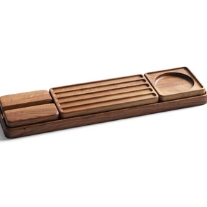 May include: A rectangular wooden desk organizer tray featuring a dark brown finish. The tray contains two small solid rectangular blocks, a central section with four parallel horizontal grooves, and a square section with a circular indentation.