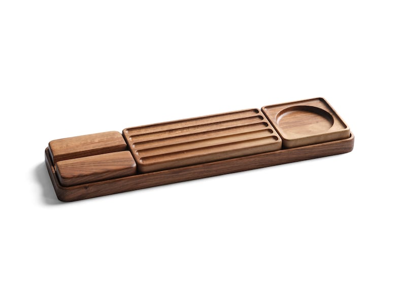 May include: A rectangular wooden desk organizer tray featuring a dark brown finish. The tray contains two small solid rectangular blocks, a central section with four parallel horizontal grooves, and a square section with a circular indentation.
