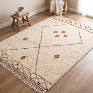 May include: A rectangular area rug featuring a cream-coloured textured pile with a large central diamond pattern outlined in thin brown lines. The design includes small mustard yellow diamond accents and brown lattice borders with white fringe.
