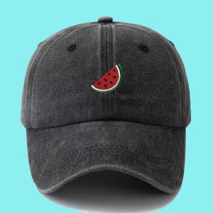 Puede incluir: Una gorra de béisbol negra con una sandía bordada en la parte delantera.