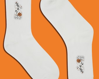 Puede incluir: Par de calcetines blancos con un diseño de Halloween. Cada calcetín tiene una pegatina con un esqueleto, una calabaza y el texto "It's the most wonderful time of the year."