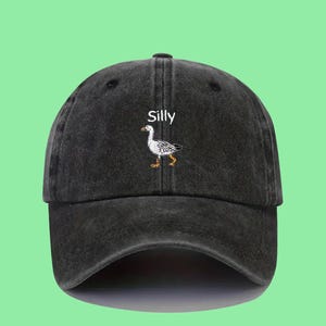Può includere: Un cappello da baseball nero in stile vintage con un'oca bianca ricamata e la parola "Silly" in bianco.