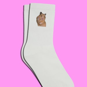 May include: White crew socks with a graphic of a hamster on the front. The hamster is brown and white and is looking to the right.