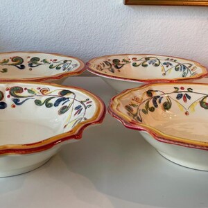 May include: Four oval ceramic serving bowls with scalloped edges. The bowls have a cream-colored interior and are decorated with a colorful floral and vine pattern. The rims are trimmed with a red and yellow border.