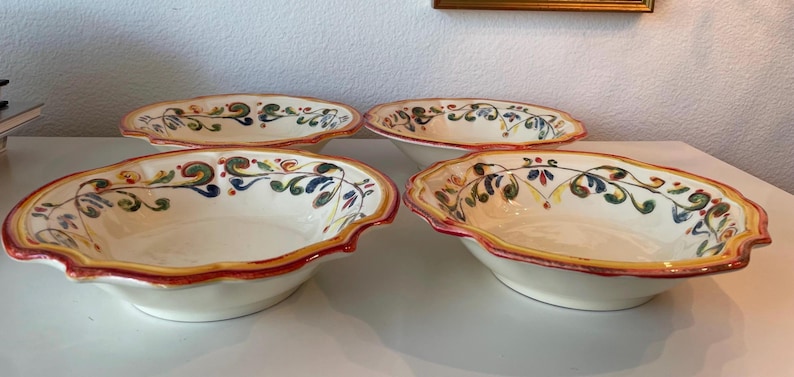 May include: Four oval ceramic serving bowls with scalloped edges. The bowls have a cream-colored interior and are decorated with a colorful floral and vine pattern. The rims are trimmed with a red and yellow border.