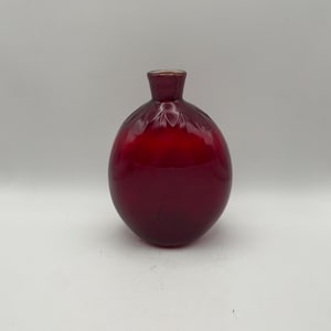 May include: A round, deep red glass vase with a narrow neck and a flared rim. The upper portion of the spherical body features a series of vertical, pressed indentations that create a subtle, petal-like pattern around the base of the neck.